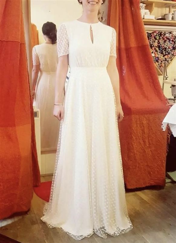 A bride in an ivory dress inside the shop, with reels of thread on the wall behind